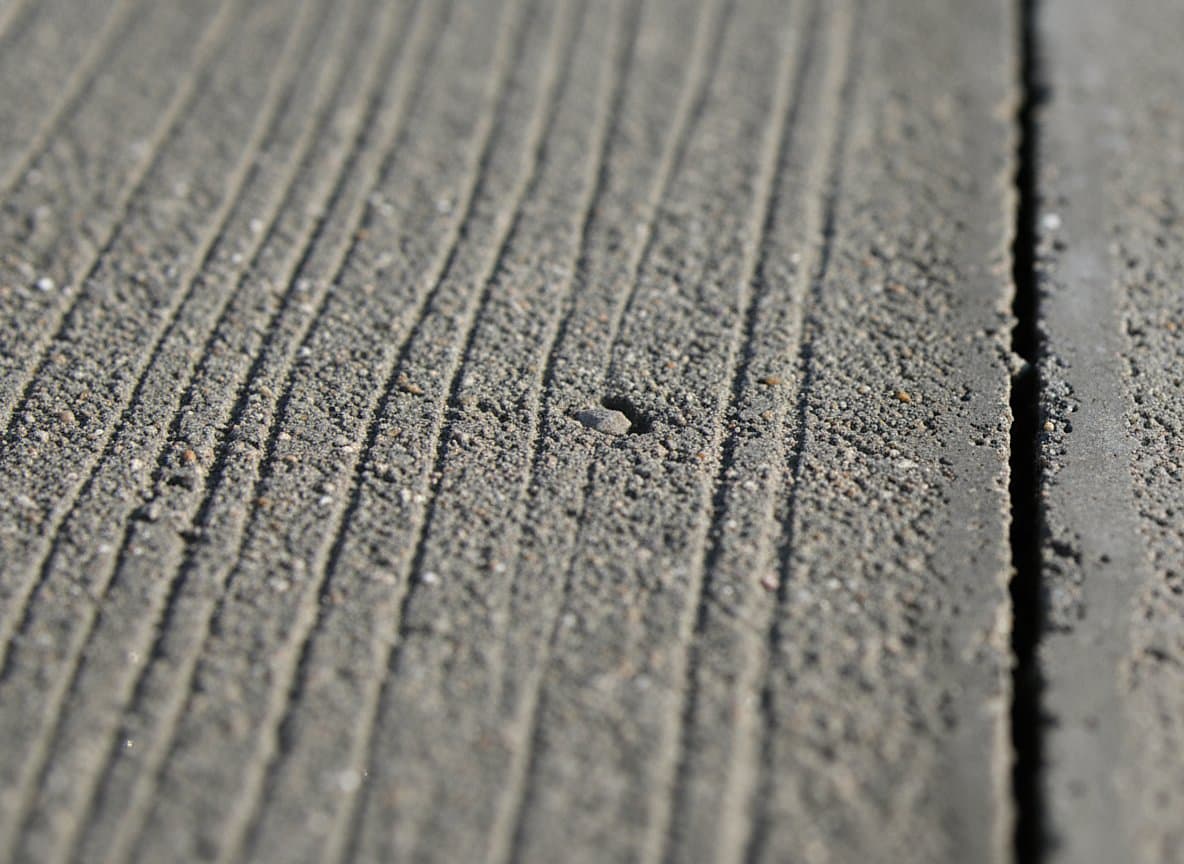 Macro of broom-finished concrete texture beside a joint.